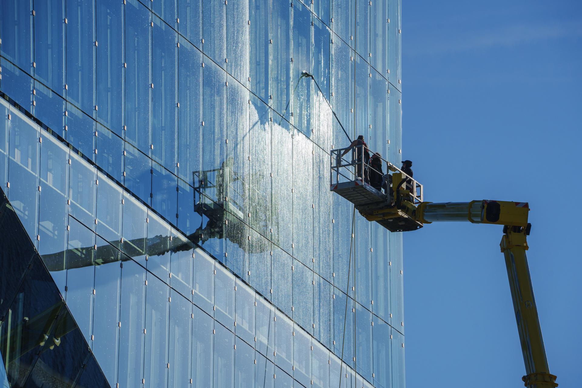 Cleaner worker using a cherry picker to clean a glas facade of a contemporary office building